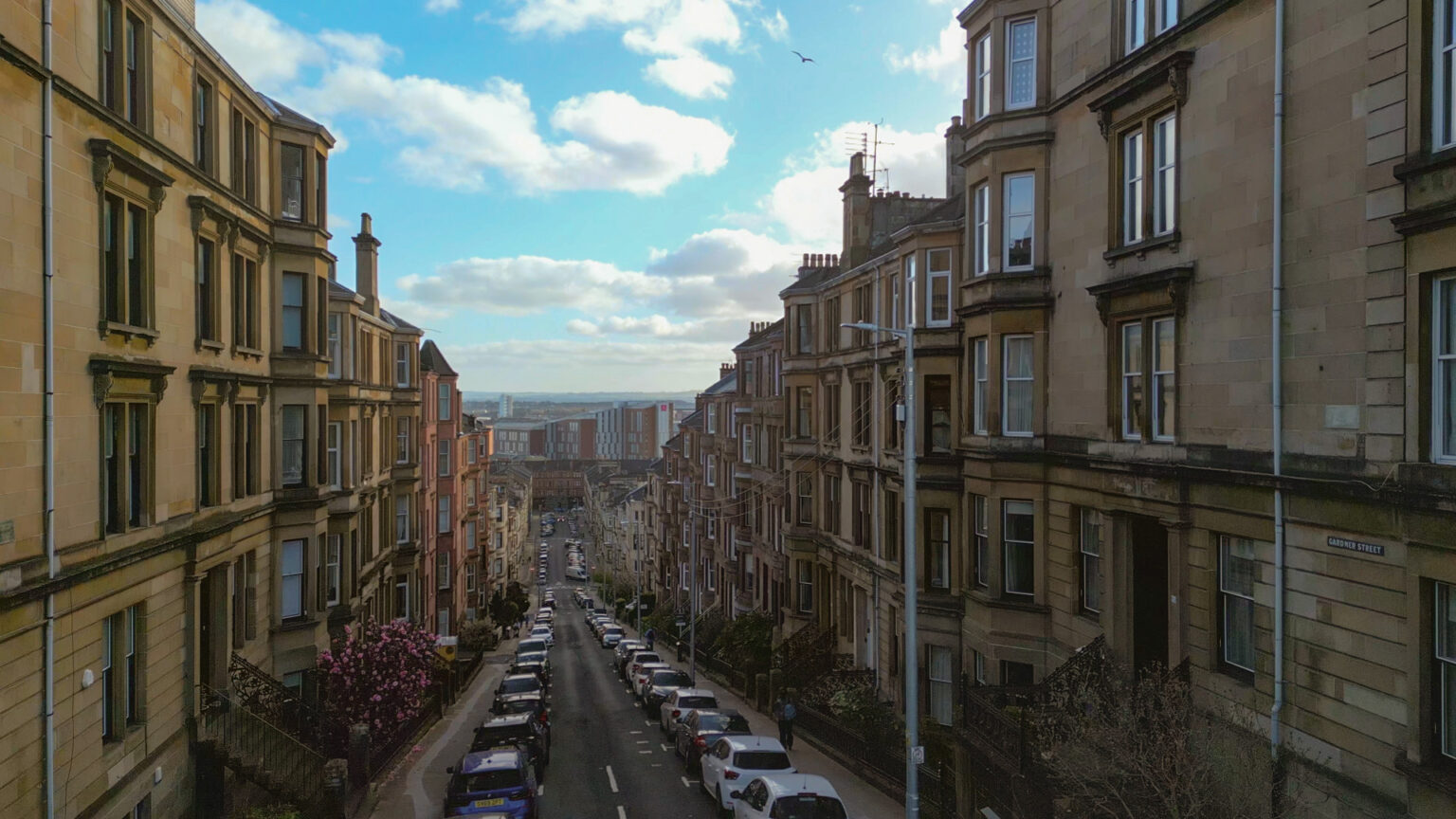Gardner Street, Partick, Glasgow looking south downhill, parked cars, blonds sandstone tenements, blue sky