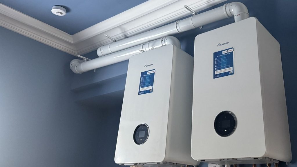 Two wall-mounted gas boilers below the ceiling cornice of a Glasgow kitchen, with a heat alarm on the ceiling