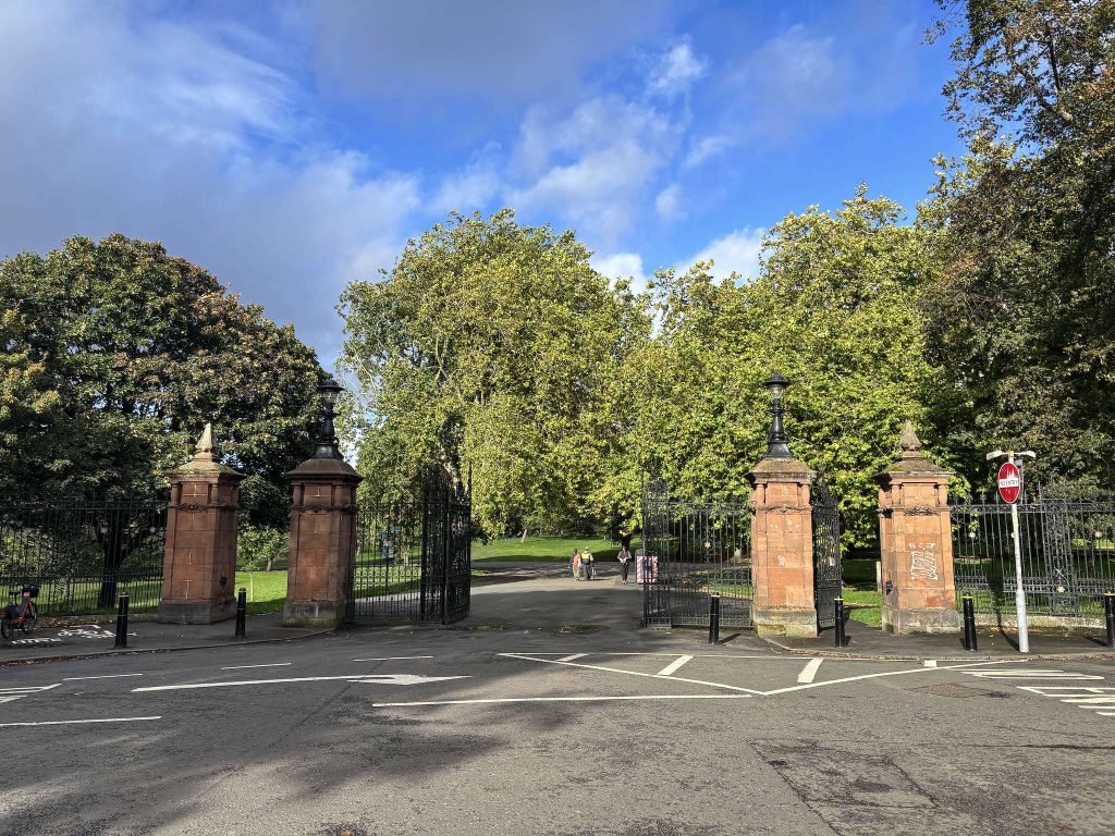 Royal Terrace, Finnieston, Glasgow, red sandstone gate piers and open iron park gates with tall trees and people walking on the path
