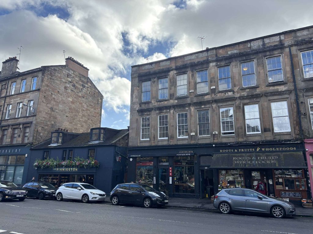 Argyle Street, Finnieston, Glasgow, The Finnieston bar with hanging flowers and Roots & Fruits wholefoods below sandstone tenements