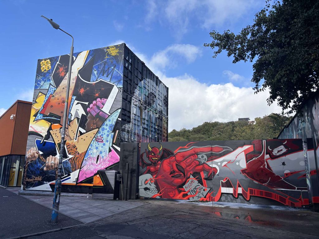 Eastvale Place, Finnieston, Glasgow, large street art murals on stacked shipping containers and a long wall painted with a red devil