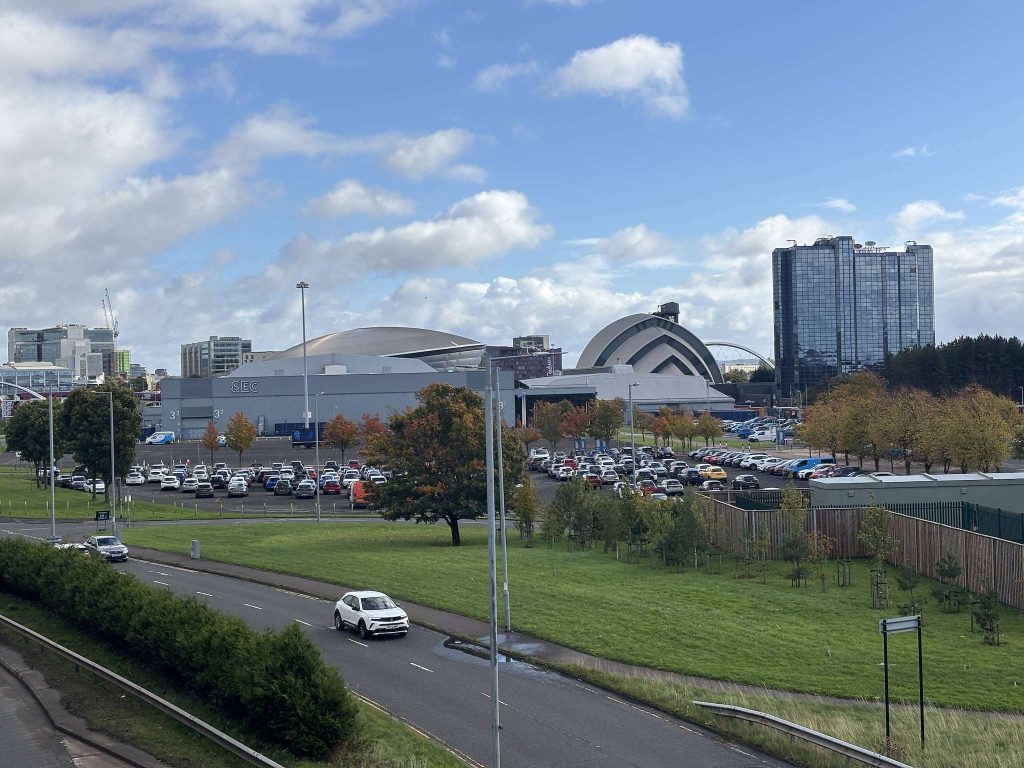 SEC and Armadillo, Finnieston, Glasgow, seen from above Eastvale Place, with a dual carriageway, busy car parks, autumn trees and a glass tower