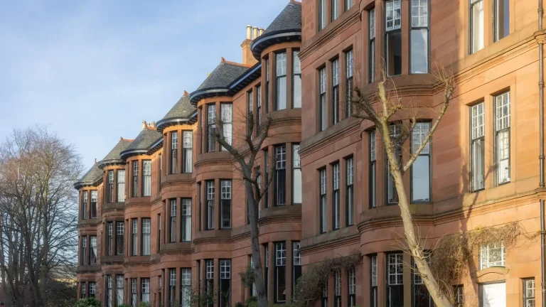 Row of red sandstone tenements with rounded bay windows on Dowanside Street in Dowanhill, Glasgow, under a clear blue sky